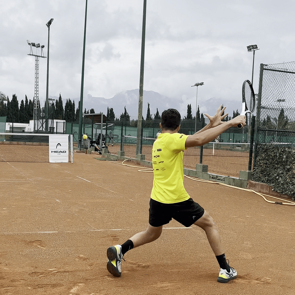 chico pegando golpe de drive desde el fondo de la pista de tenis